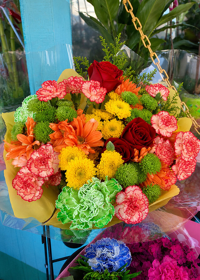 Bright hand-tied bouquet of orange gerberas, red roses and green carnations at the Blossoms Flower Shop stand in San Diego